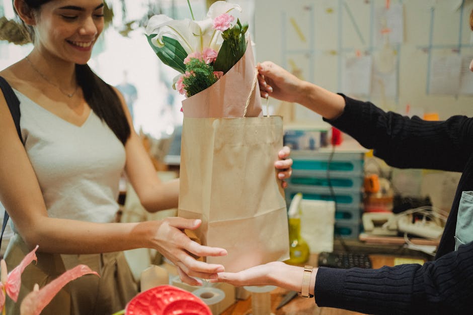 A floral delivery scene showing a woman with long dark hair and a white sleeveless top receiving a bouquet of fresh flowers from a staff member at Florist Streatham. The bouquet features white lilies